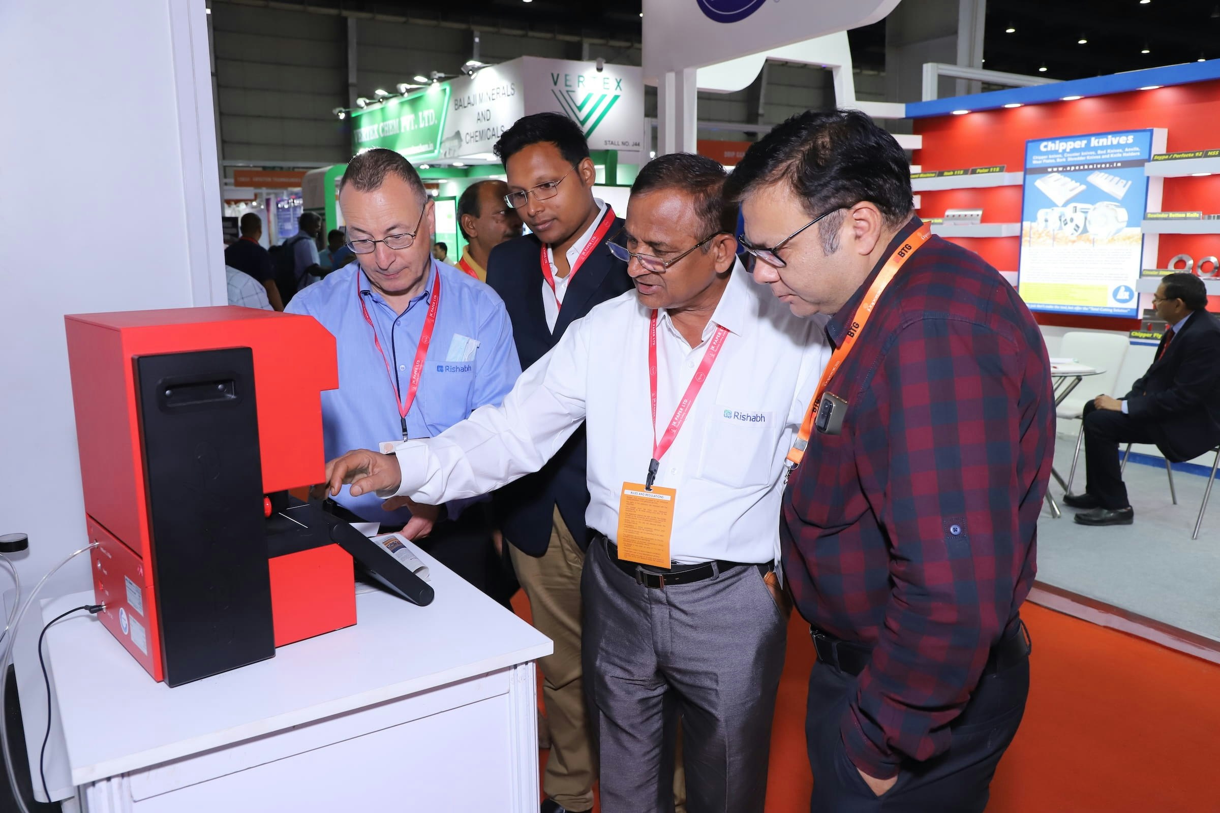 Group of professionals examining a red device at a trade show exhibition.