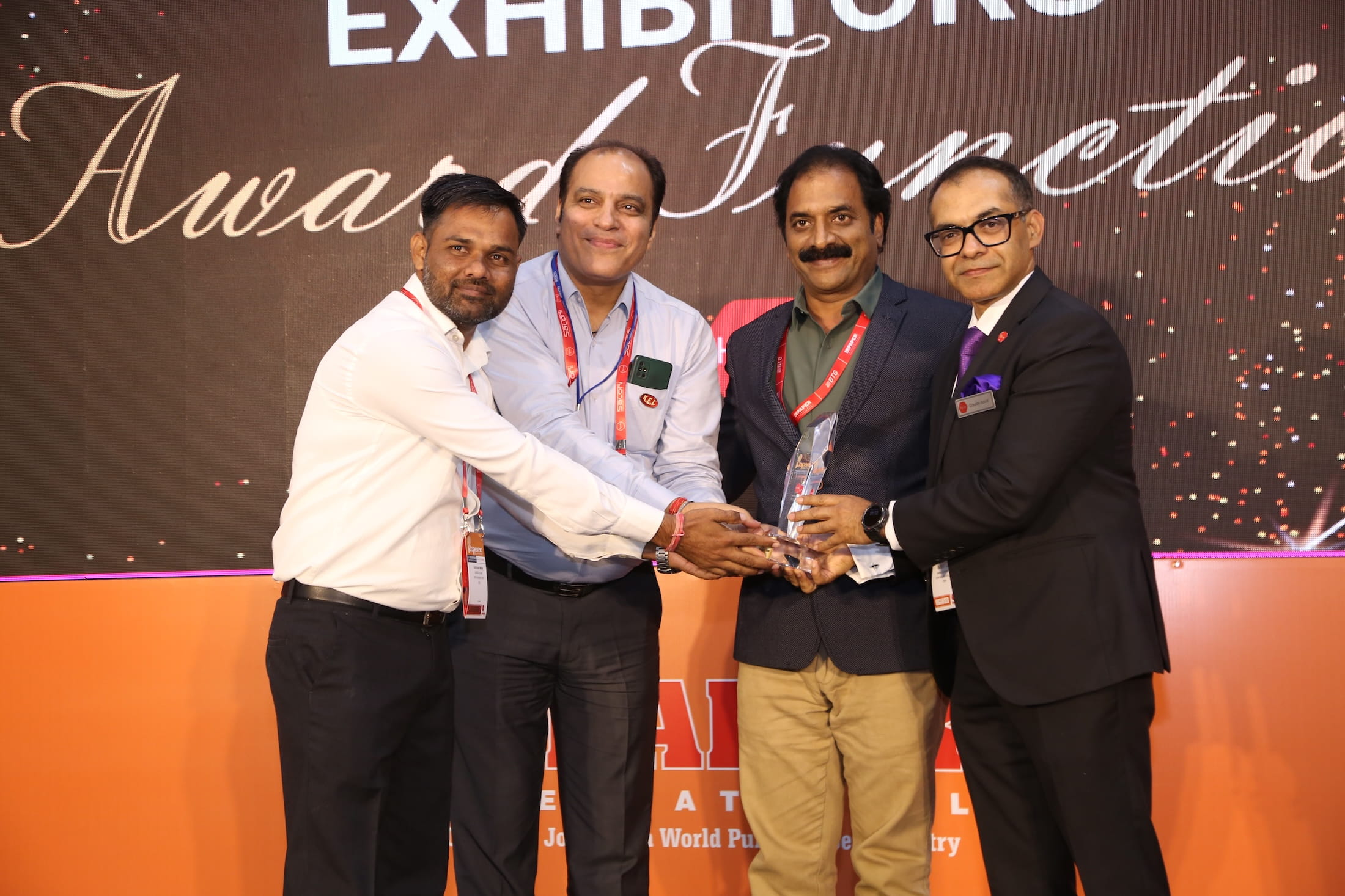 Four attendees celebrating their award on stage in the awards section, with the event’s awards-themed backdrop at Paperex South India.