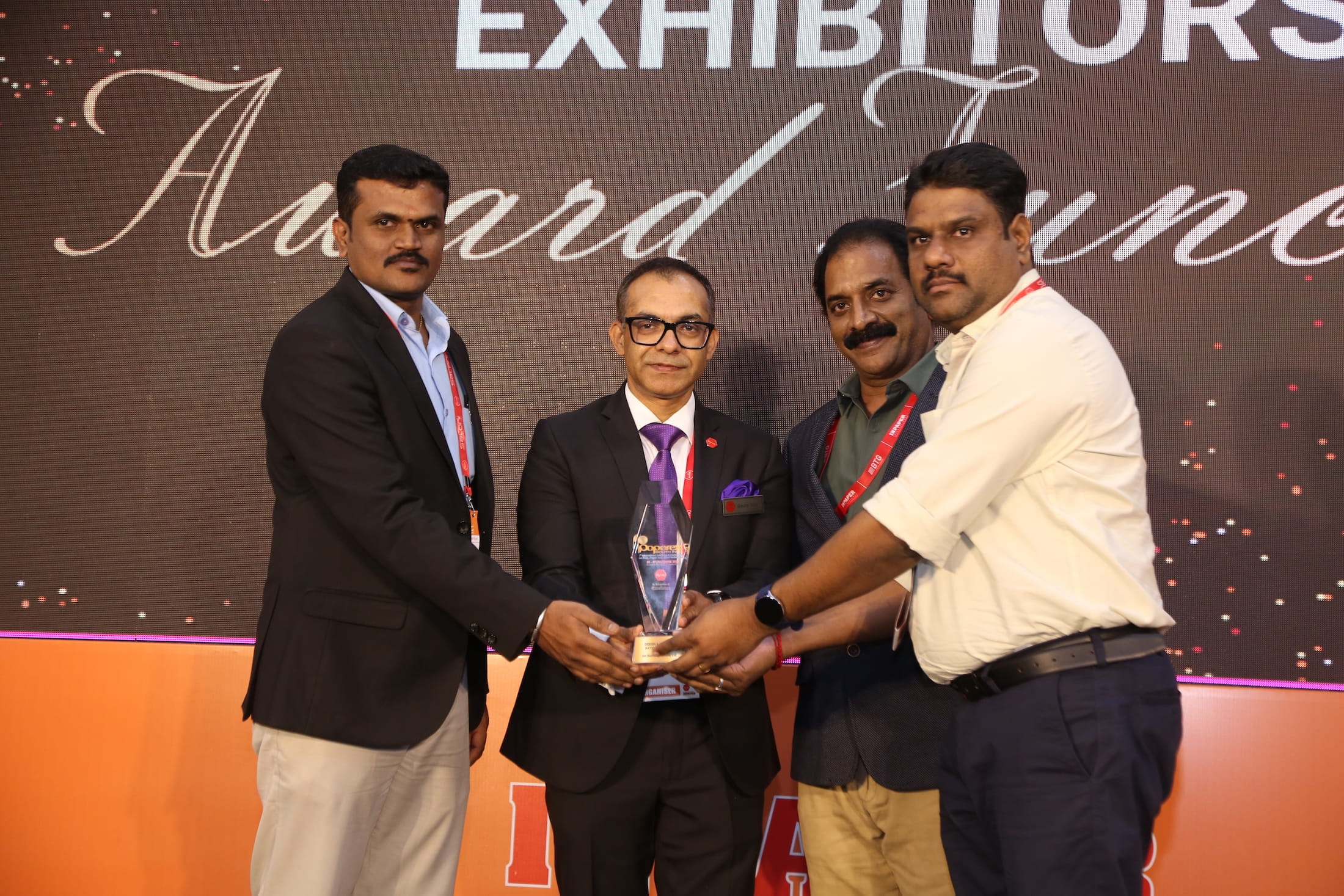 Another group of four attendees celebrating their award on stage, with the awards section backdrop behind them at Paperex South India