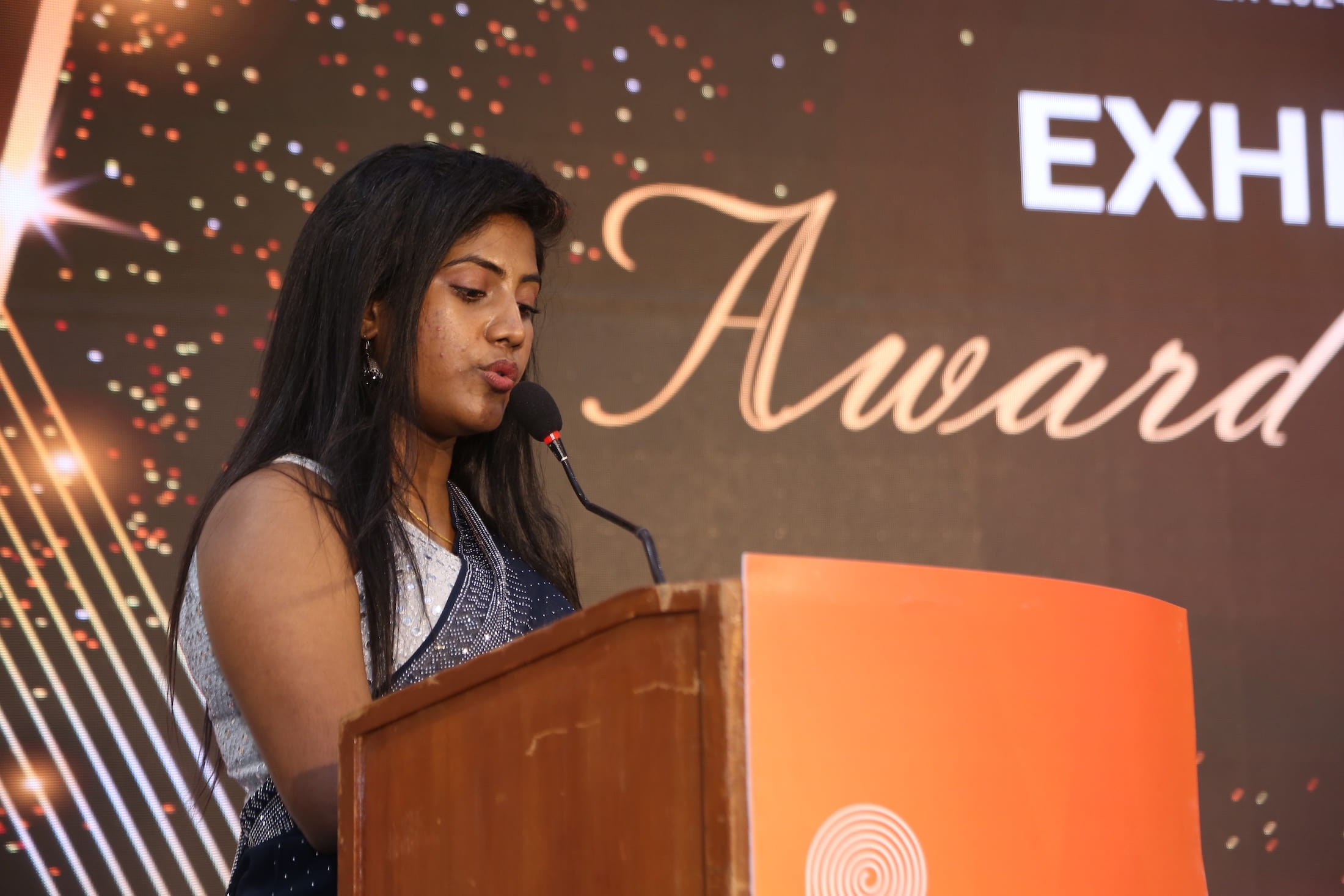 Woman delivering a speech at the podium during an awards ceremony at Paperex South India.