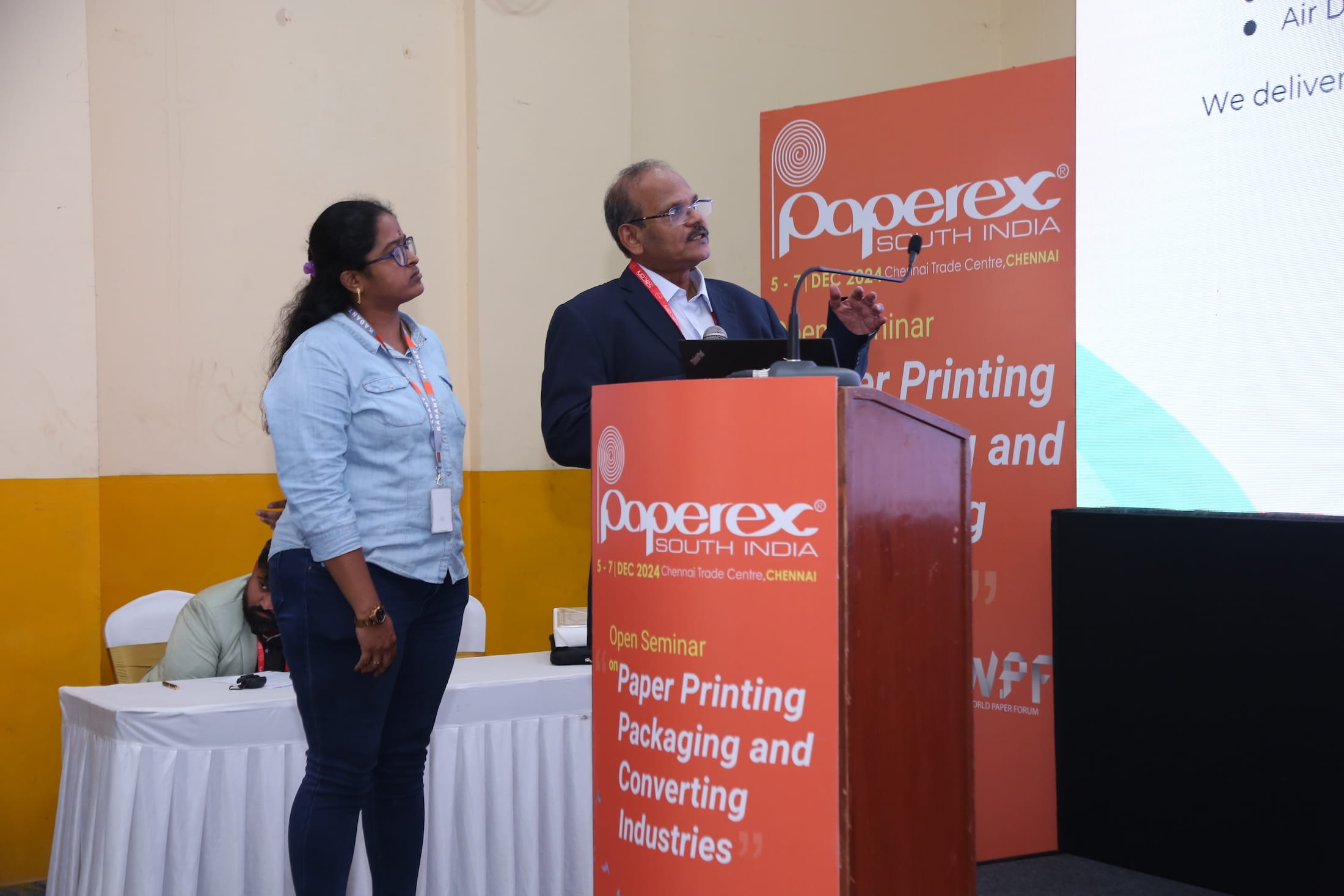 Man speaking at Paperex South India seminar podium with woman standing nearby.