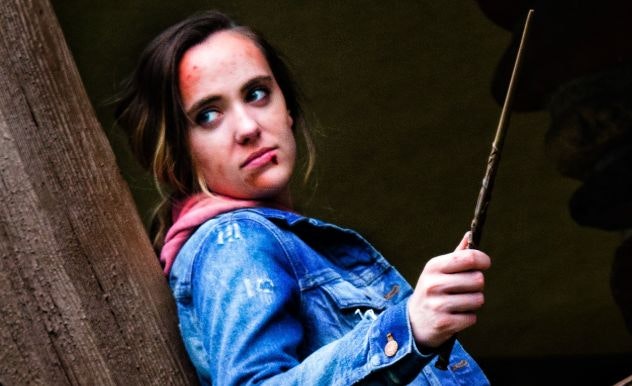 Cosplayer dressed in a jean jacket holding a wand like Hermione