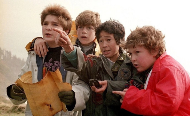 The Goonies read a map and check either compass as they set off on their adventure.