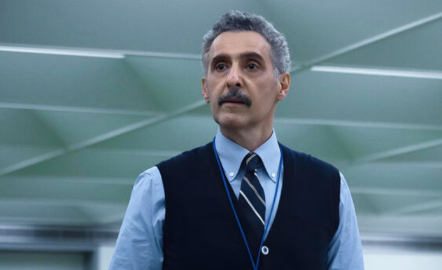 Irving stands in the office, looking inquisitively at someone off screen