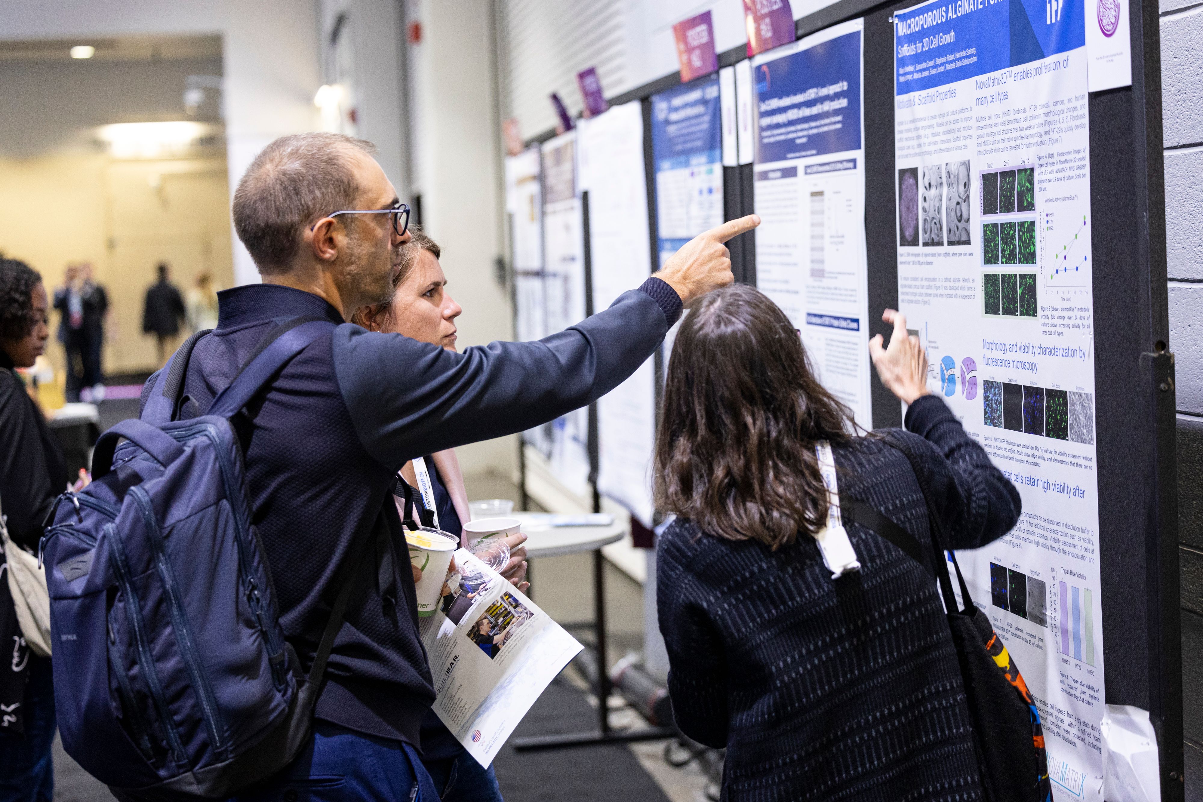 Bioprocessing professionals point at the poster wall at BioProcess International (BPI) part of BioTech Week Boston.