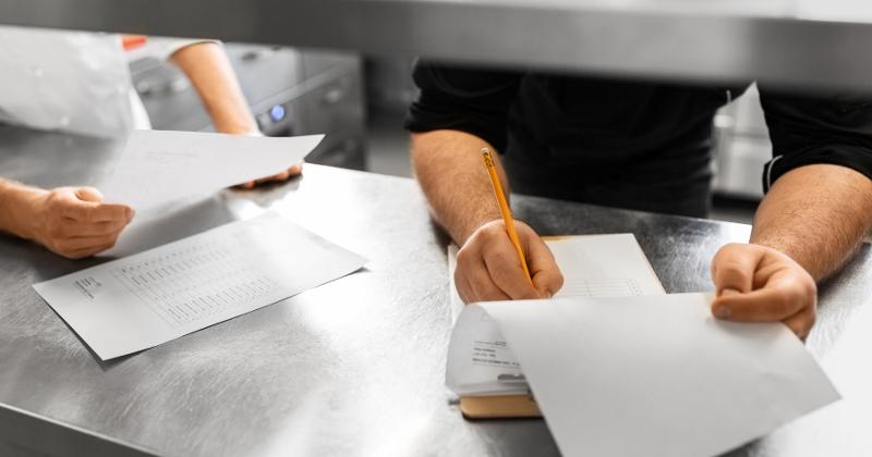 Restaurant employees fill out inventory sheets on a stainless steel counter