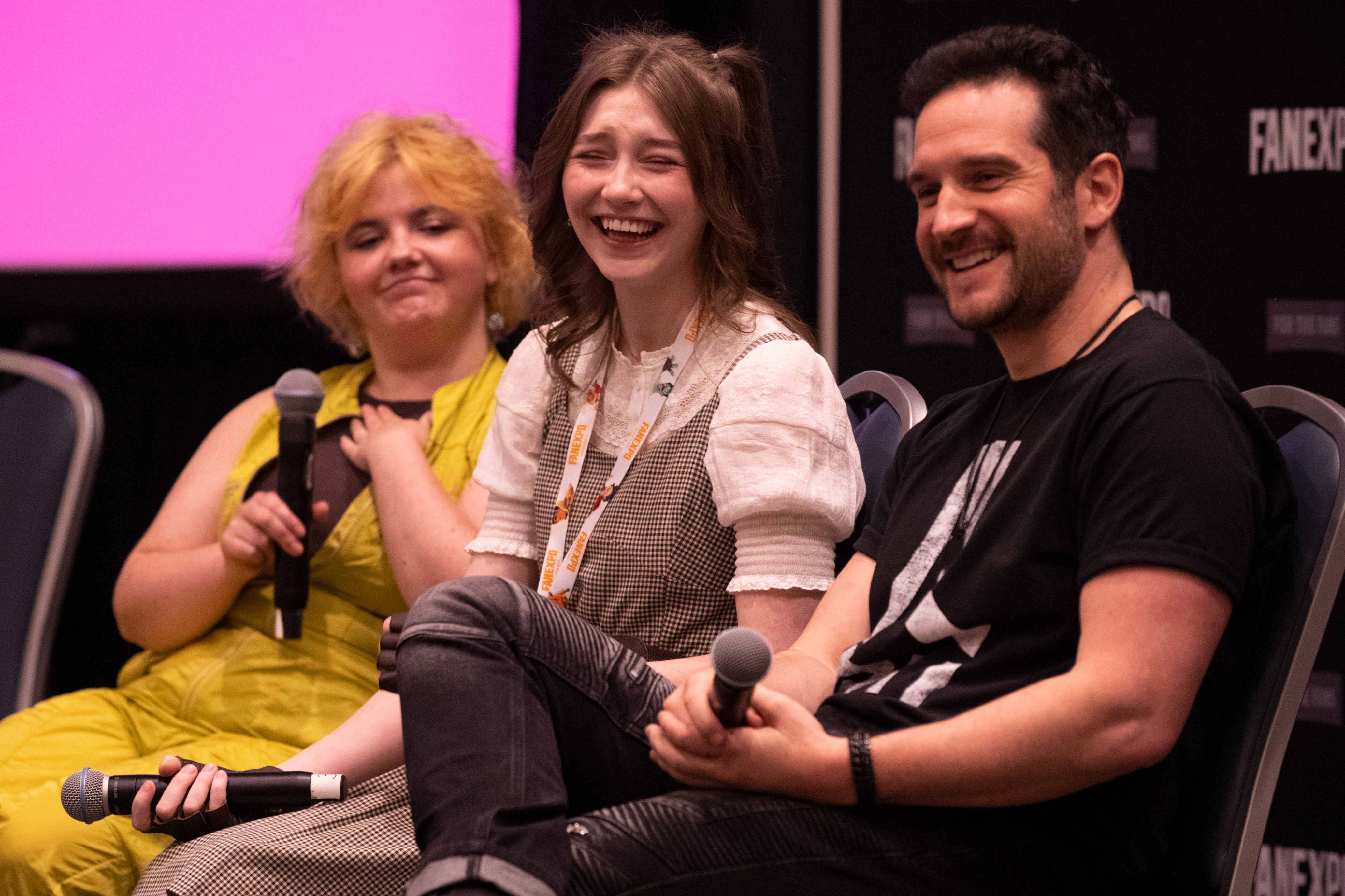 The Helluva Boss cast sits on stage in front of a large audience, laughing and chatting with fans during their panel.