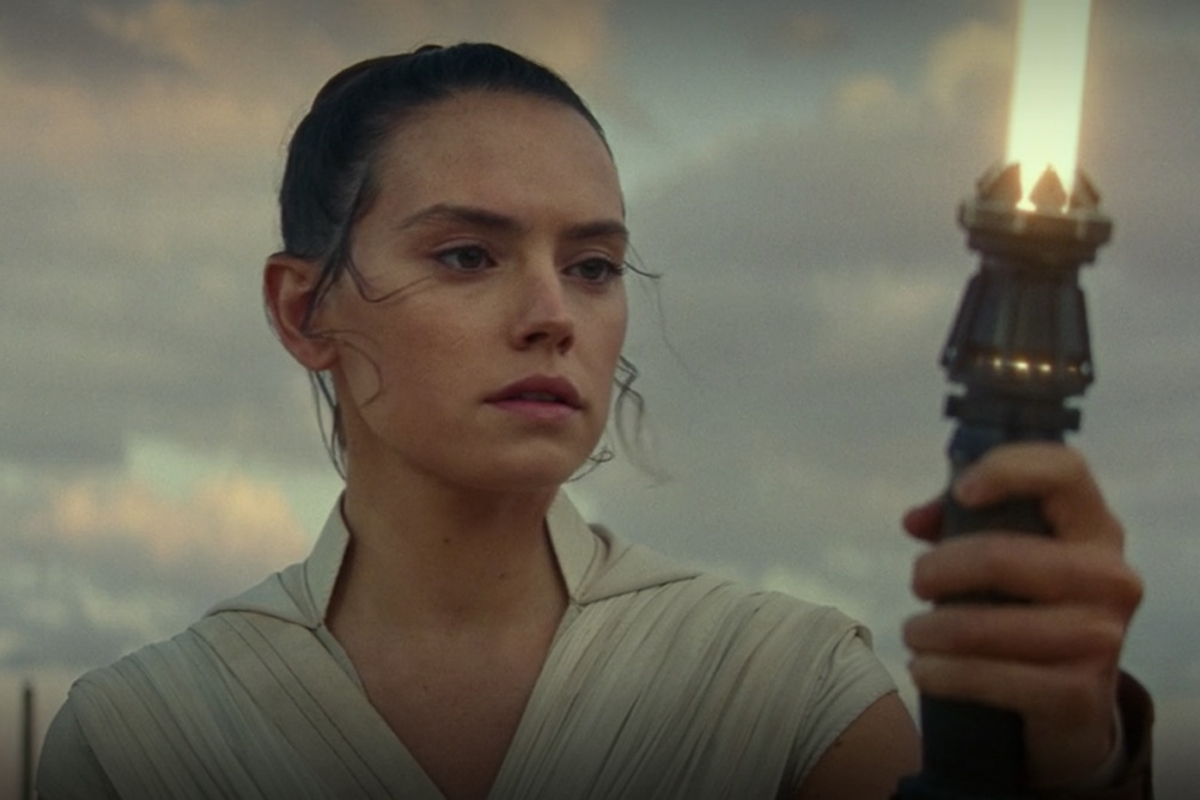 Rey Skywalker looking intently at an ignited yellow lightsaber she's holding
