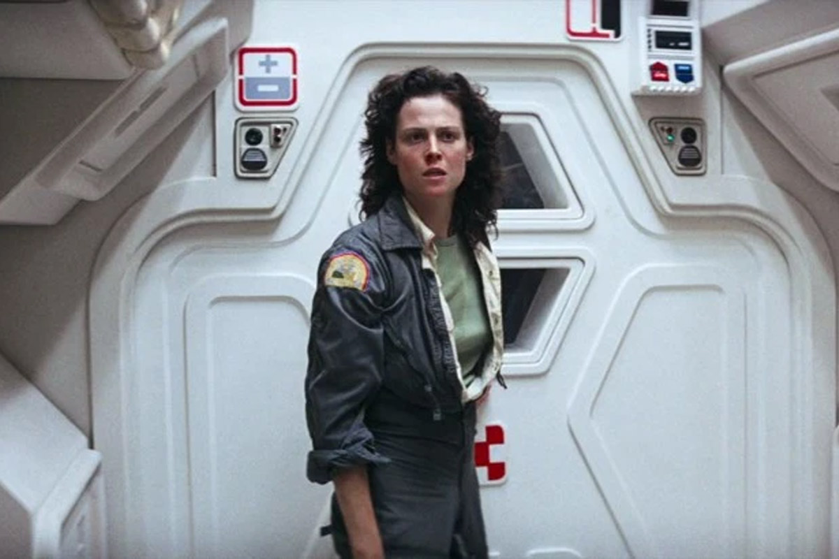 Ripley stands on a ship in a grey outfit