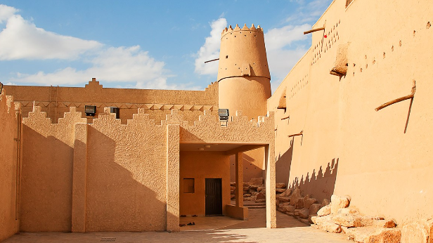 Entrance to a traditional adobe fort with a tower under a clear sky.