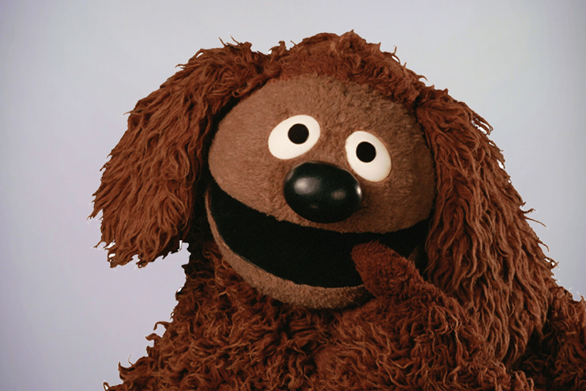 Muppet character Rowlf standing with a finger in his mouth on a grey background