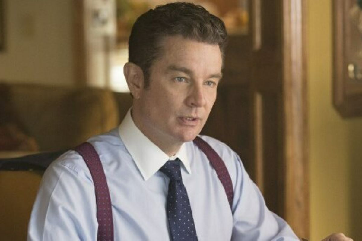 James Marsters sitting in a kitchen wearing plum suspenders, a dress shirt and a blue tie