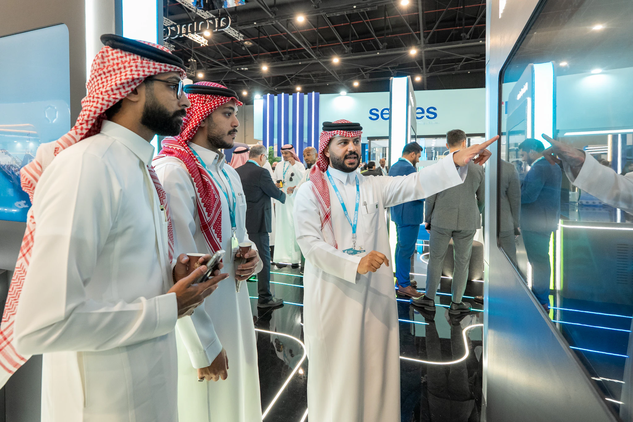 three man in traditional arabic dress looking at display at exhibition