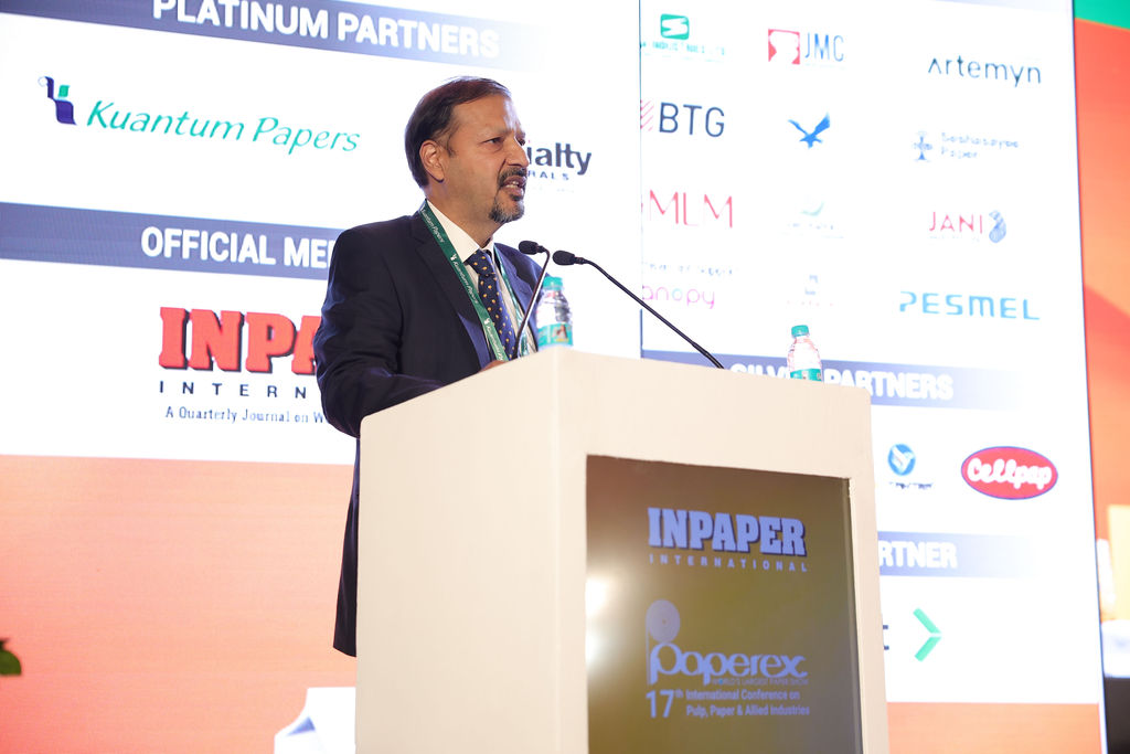 Man speaking at a paper industry conference podium with sponsor banners displayed