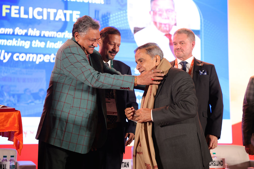 Three men seated at a conference panel with name plates and floral decorations