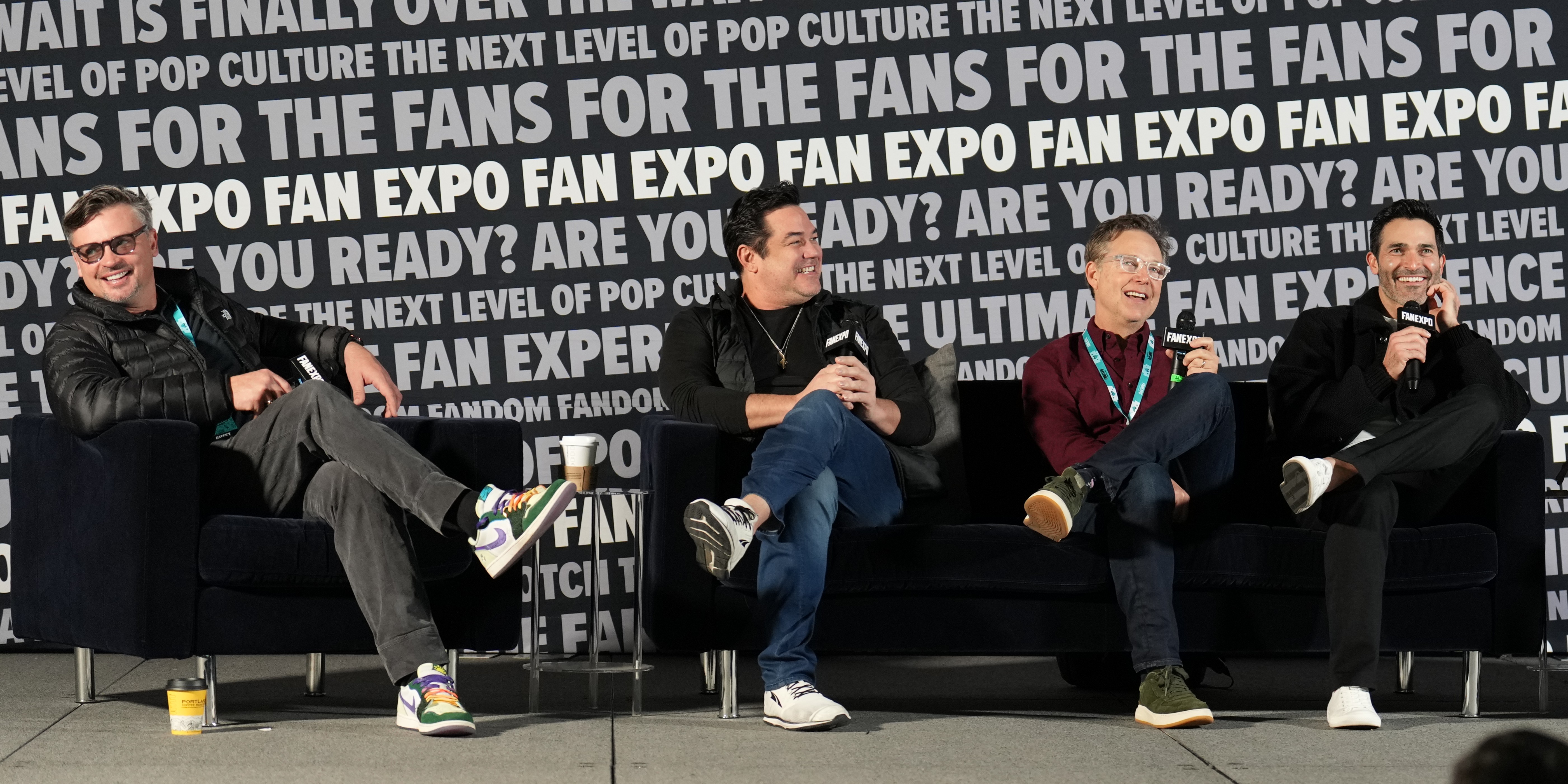 Tom Welling, Dean Cain, George Newbern, and Tyler Hoechlin sit on a stage at a FAN EXPO panel, laughing and engaging with the audience. The backdrop reads “FAN EXPO” repeatedly, creating an exciting and immersive pop culture atmosphere.