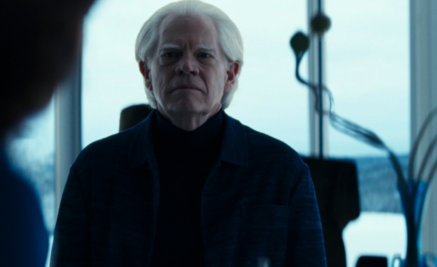 A white haired man stares with an angry expression at a shadowed person in the foreground. They are standing in a very modern office.