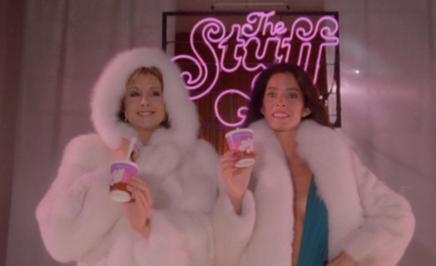 Models, wearing white fluffy parkas, pose with personal sized tubs of 'The Stuff', in front of a pink neon sign of the product name.