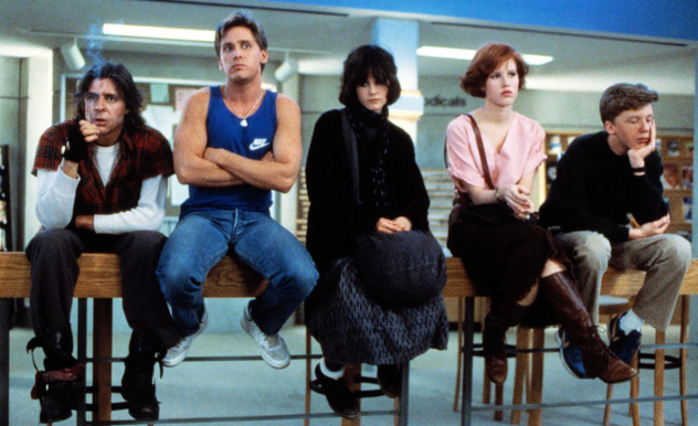 The Breakfast Club are seated on one of the library's long tables - each with a look of distaste on their faces for being in detention. 