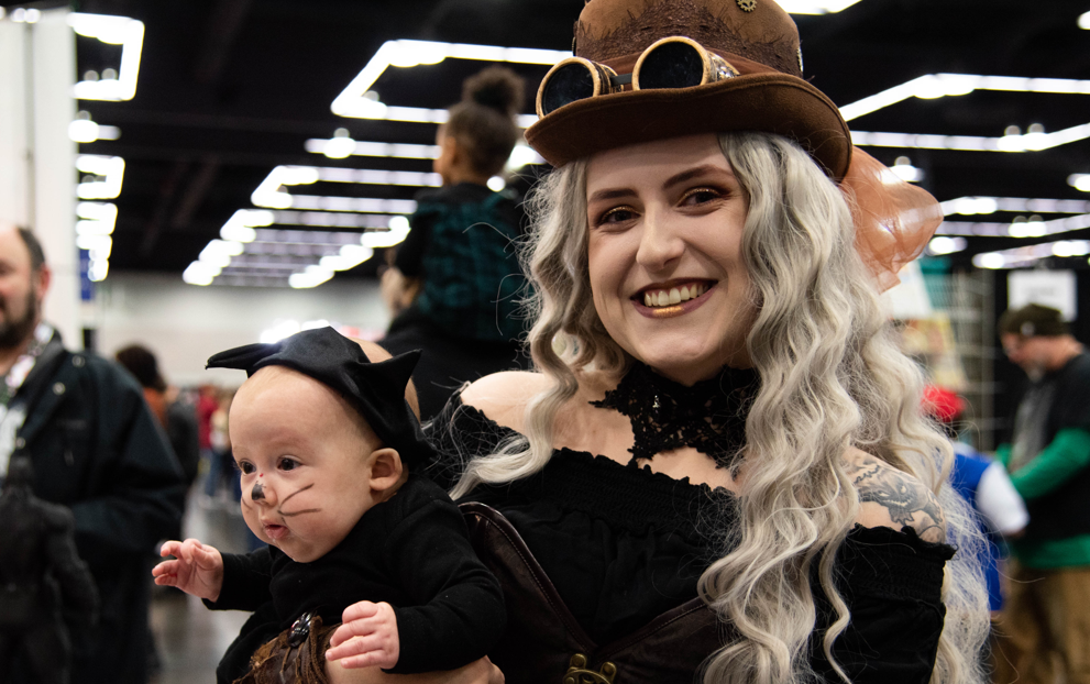 A mother and her child dressed up together - She is dressed as a steampunk witch, and her baby is a little black cat