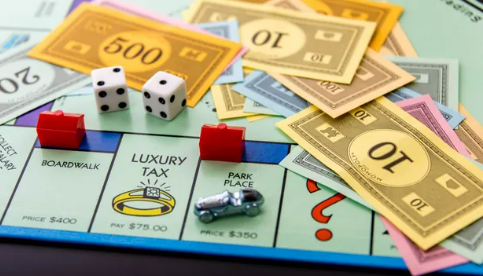A monopoly board in play. The car is on Park Place, where a house has been purchased. Monopoly money of all amounts is scattered on the board.