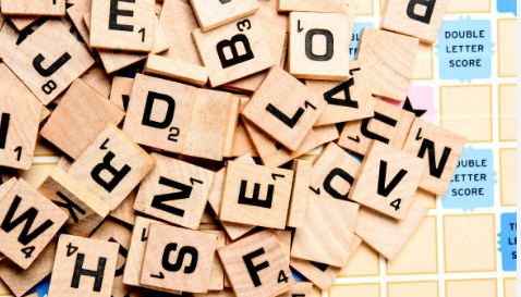 A pile of scrabble tiles is dumped over a board, with letters facing both upright and downward. Two "Double Word Score" spots are visible on the far right.