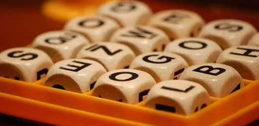 A boggle board with upturned letters S, Qu, O, G, E, Z, W, E, O, G, O, S, L, B, H.