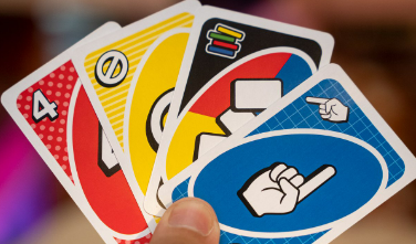 Under a thumb, there are 4 uno cards, a red 4, a yellow skip card, a wild card, and a blue card with a finger giving the number 1