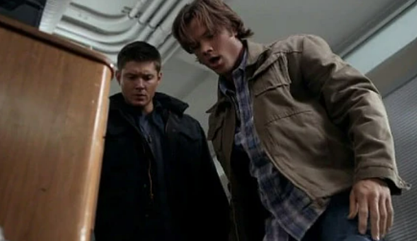 Sam and Dean Winchester stare into an open desk drawer. The brothers stare in horror and awe at what they've found. 