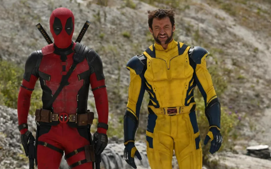 Deadpool and Wolverine, in their classic, comic style suits, walk through the desert while in conversation.