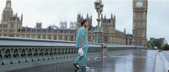 Cillian Murphy, dressed in blue scrubs, walks a rain covered bridge in a barren London, UK.