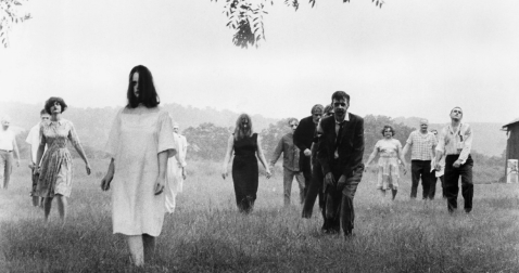 In black and white, a hoard of zombies walk toward the camera through an otherwise empty field.