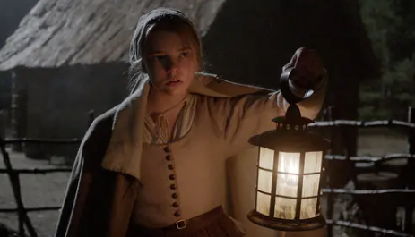 Thomasin, looking slightly disheveled, carries a lantern into the darkness. She looks fearful as she explores the farm.