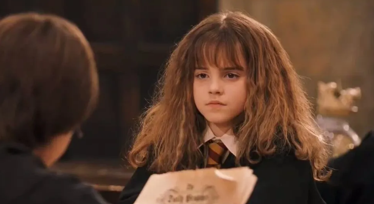 A young Hermoine stares down George Weasley sternly as he reads.