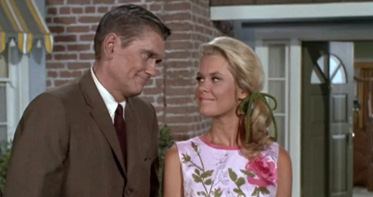 Darrin and Samantha Stephens stand outside their home. They smile to each other in agreement.