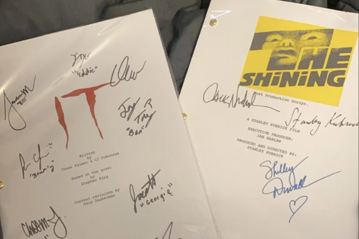 Scripts for IT and The Shining lay on a bed with multiple autographs on them both