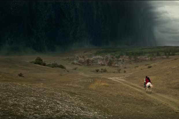 A character in black and red rides a horse down a long empty trail towards a black cloud