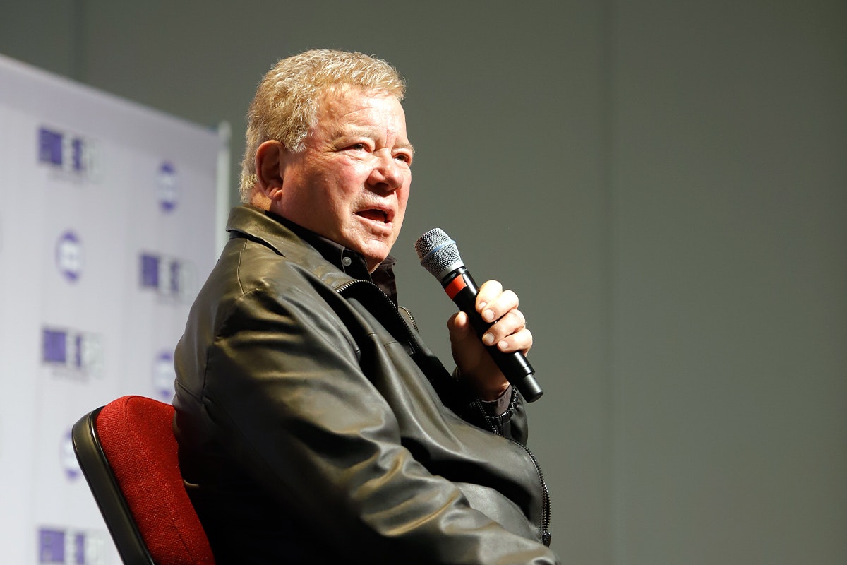 William Shatner holds a microphone and speaks on stage