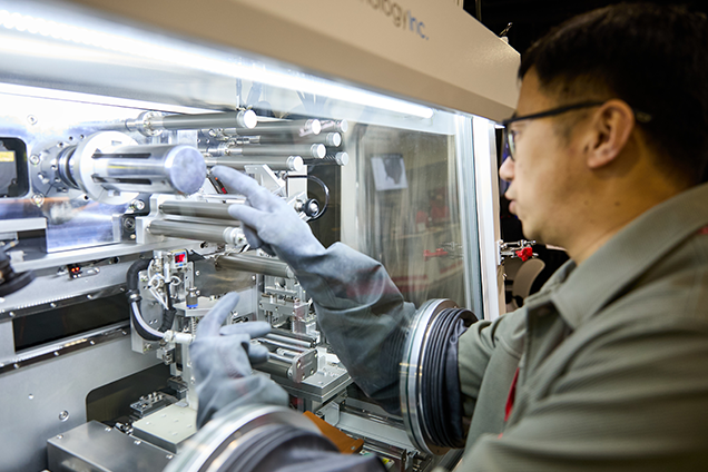 A man in a lab coat operates a complex machine, focused on his work in a laboratory setting.