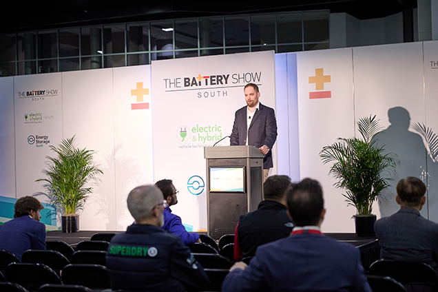 A man stands at a podium, delivering a speech to an audience at The Battery Show conference