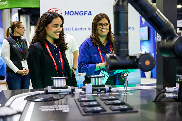 Two women stand beside a robot at The Battery Show