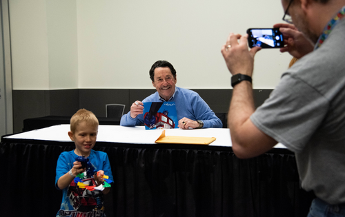 Voice Actor Peter Cullen taking a photo with a young boy with blonde hair.