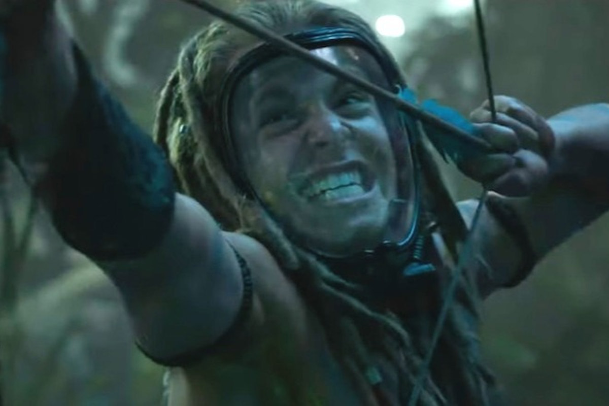 A man with a clear face mask and bow and arrow looks angry as he readies the arrow