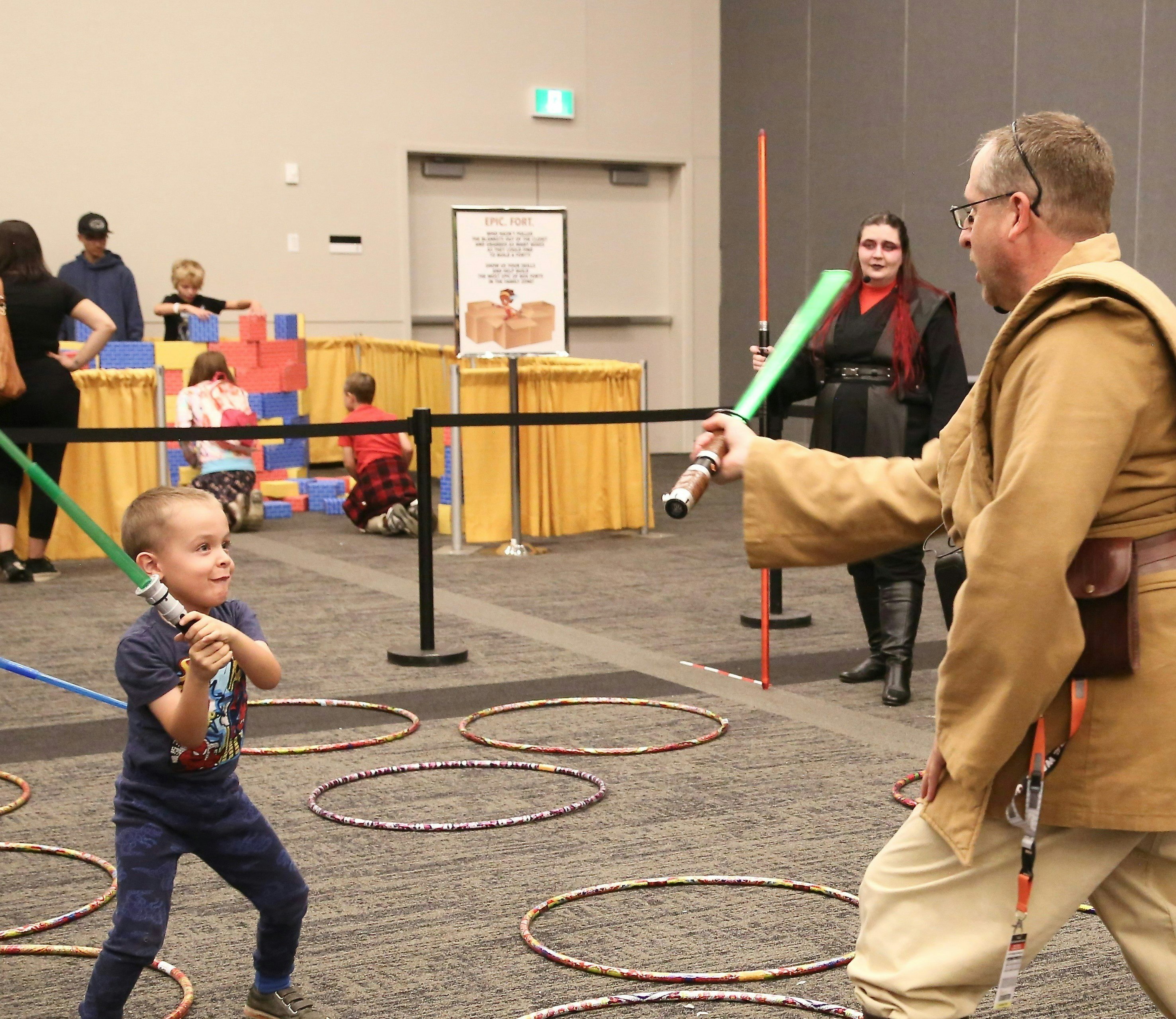 Boy holding a green lightsaber fighting a Jedi with a green light saber.