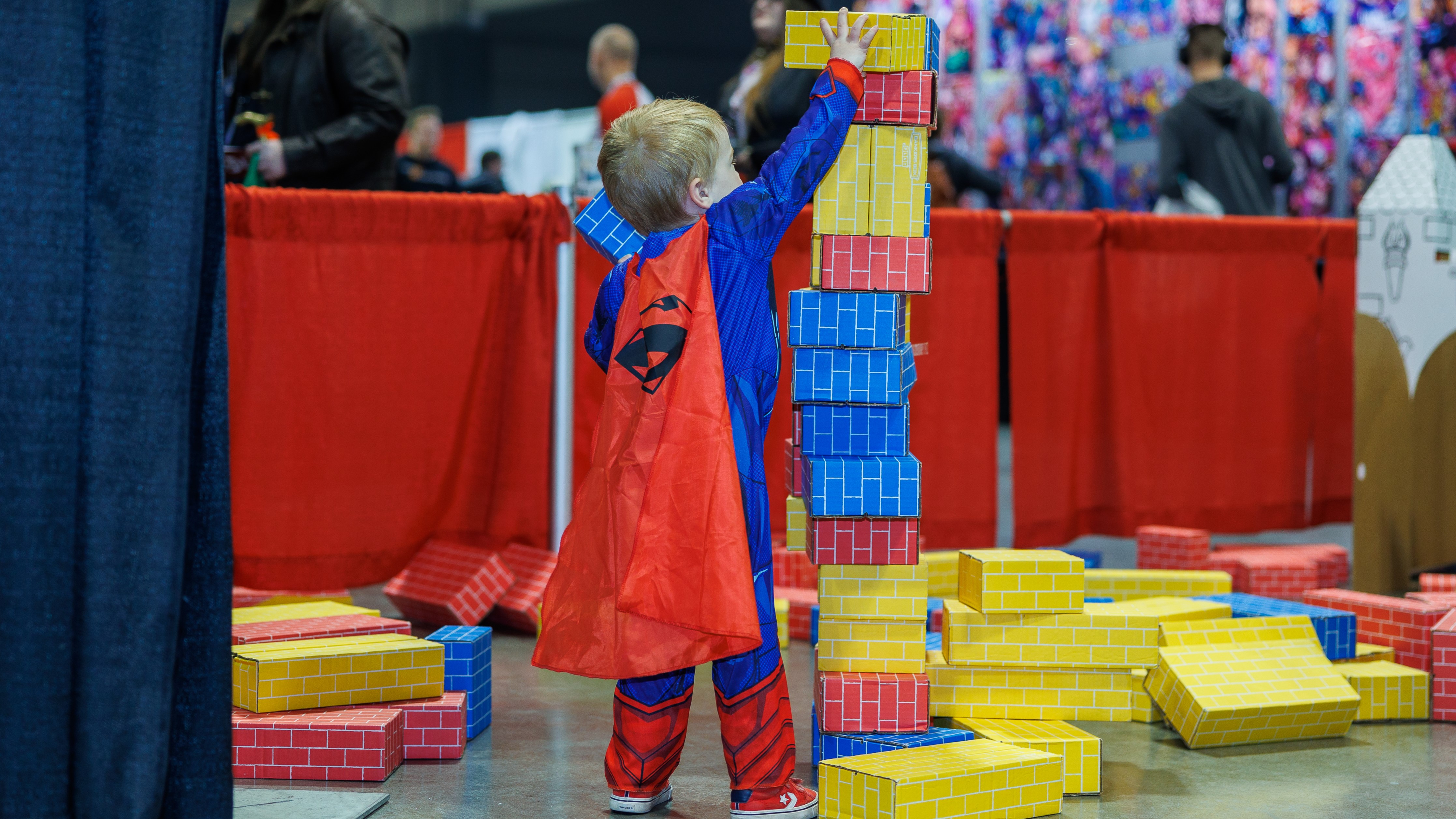A little superman stacks fake bricks in the family zone