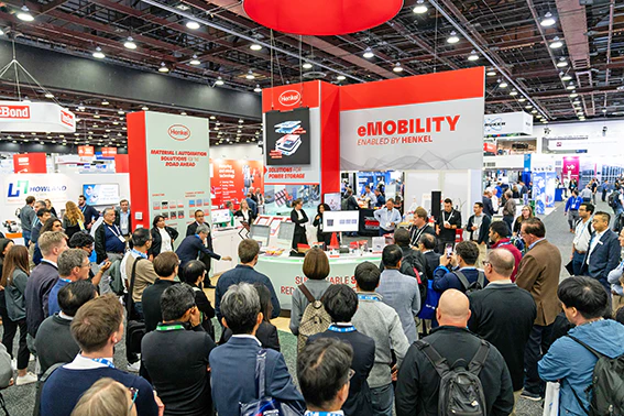A large group of people gathered around a booth, engaging in conversation and examining displayed items