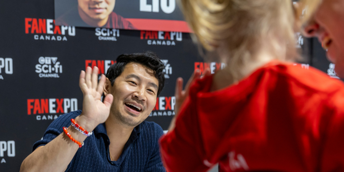 Simu Liu smiles and waves to a little girl in her parents arms. Her little hand waves back.
