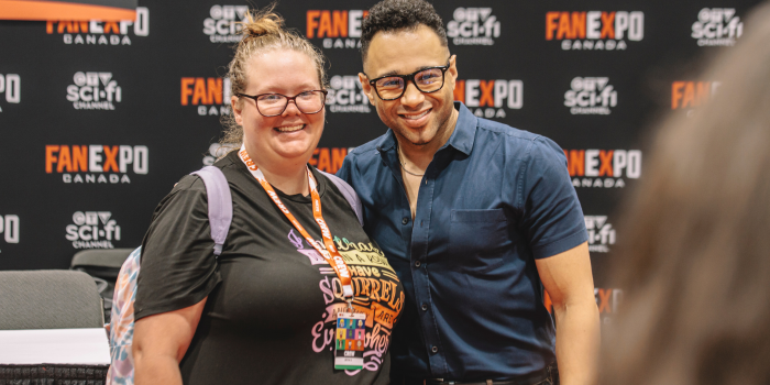 Corbin Bleu stands and poses with a fan for a picture. Both smile as a volunteer takes the photo in the foreground.
