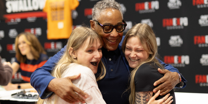 Giancarlo Esposito holds two fans tightly in a hug. All three have wide, joyous smiles as they pose excitedly for the photo.