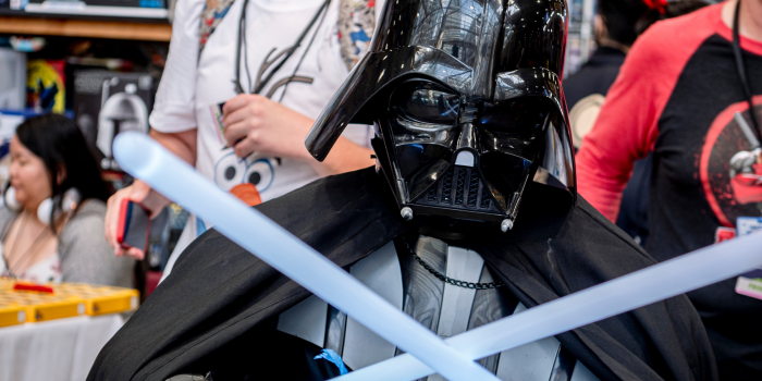 Darth Vader poses, duel-wielding light sabers as fans pass.